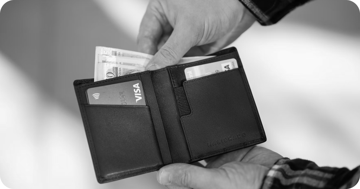 Imagen en blanco y negro de dos manos que sostienen una billetera donde se observa dos tarjeta de crédito Visa y dinero en efectivo